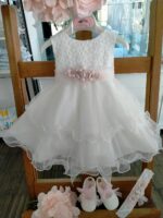 Abito Dalia Mimilù Abito da cerimonia e Battesimo color latte, modello senza maniche in misto cotone con gonna in tulle multistrato e ampia sottogonna, elegante corpino ricamato, cintura in organza color rosa tenue -annodabile sul retro con un grande fiocco e ampi lembi - completata da una raffinata spilla floreale rosa polvere con dettagli in pizzo. Abito da Battesimo Abito da Cerimonia Neonata
