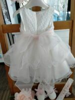 Abito Dalia Mimilù Abito da cerimonia e Battesimo color latte, modello senza maniche in misto cotone con gonna in tulle multistrato e ampia sottogonna, elegante corpino ricamato, cintura in organza color rosa tenue -annodabile sul retro con un grande fiocco e ampi lembi - completata da una raffinata spilla floreale rosa polvere con dettagli in pizzo. Abito da Battesimo Abito da Cerimonia Neonata