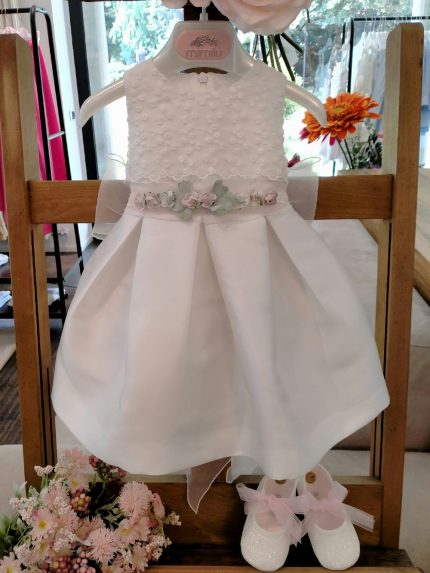 Abito Camelia Mimilù Abito da cerimonia e Battesimo color latte, modello senza maniche in mikado con ampia sottogonna ed elegante corpino ricamato applicato, cintura in organza color rosa tenue - annodabile sul retro con un grande fiocco e ampi lembi - completata da una raffinata spilla floreale rosa polvere e verde con dettagli in organza. Abito da Battesimo Glam Abito da Cerimonia Neonata