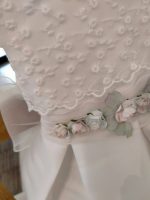 Abito Camelia Mimilù Abito da cerimonia e Battesimo color latte, modello senza maniche in mikado con ampia sottogonna ed elegante corpino ricamato applicato, cintura in organza color rosa tenue - annodabile sul retro con un grande fiocco e ampi lembi - completata da una raffinata spilla floreale rosa polvere e verde con dettagli in organza. Abito da Battesimo Glam Abito da Cerimonia Neonata