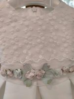 Abito Camelia Mimilù Abito da cerimonia e Battesimo color latte, modello senza maniche in mikado con ampia sottogonna ed elegante corpino ricamato applicato, cintura in organza color rosa tenue - annodabile sul retro con un grande fiocco e ampi lembi - completata da una raffinata spilla floreale rosa polvere e verde con dettagli in organza. Abito da Battesimo Glam Abito da Cerimonia Neonata
