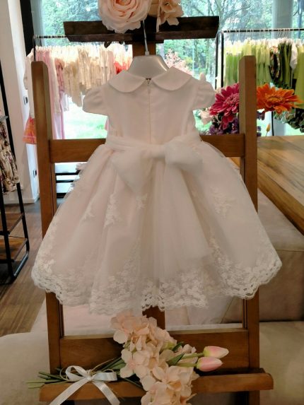 Abito Peonia Mimilù Abito da cerimonia e Battesimo color latte, modello con colletto e manichine corte, corpino in tessuto di cotone doppiato in tulle, ampia gonna in elegante pizzo debrodè con doppia sottogonna in tulle/cotone, chiusura con zip invisibile sul retro. Nastro color latte in vita con applicazione floreale removibile e maxi fiocco sul retro. Abito da Battesimo Glam Abito da Cerimonia Neonata